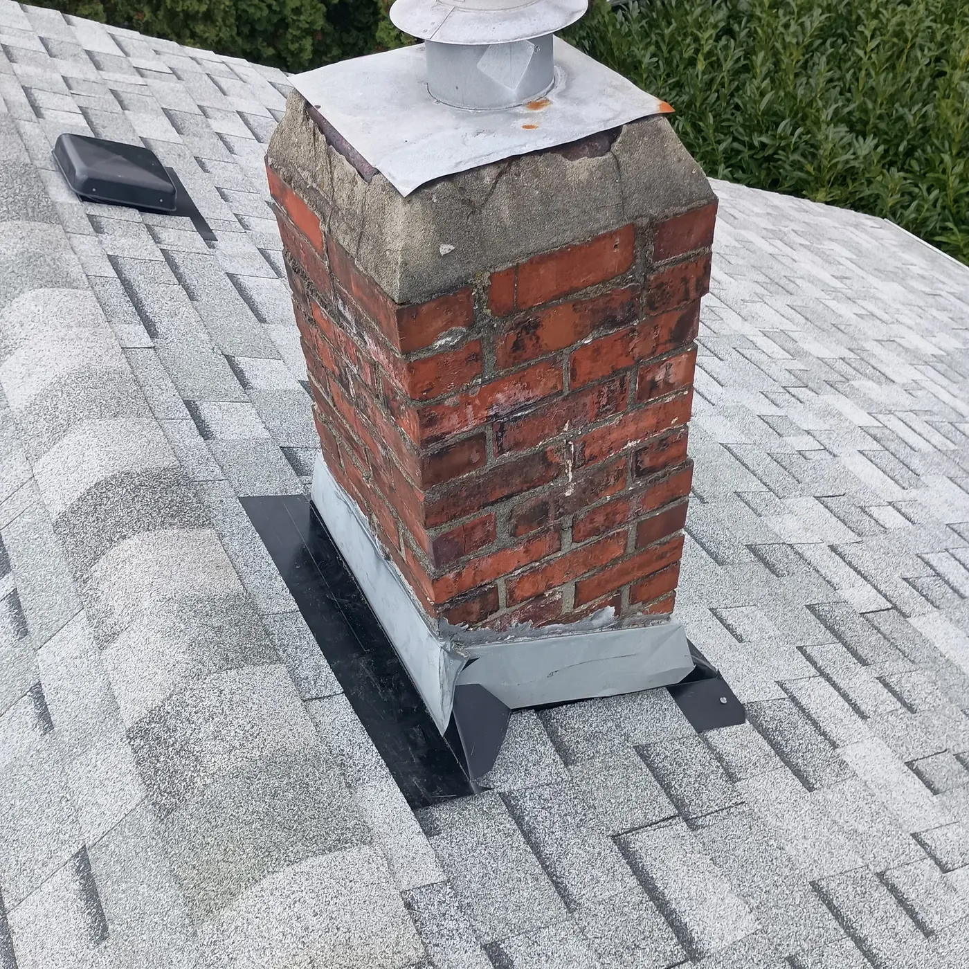 New step flashing and counter-flashing installed around a brick chimney on a shingle roof