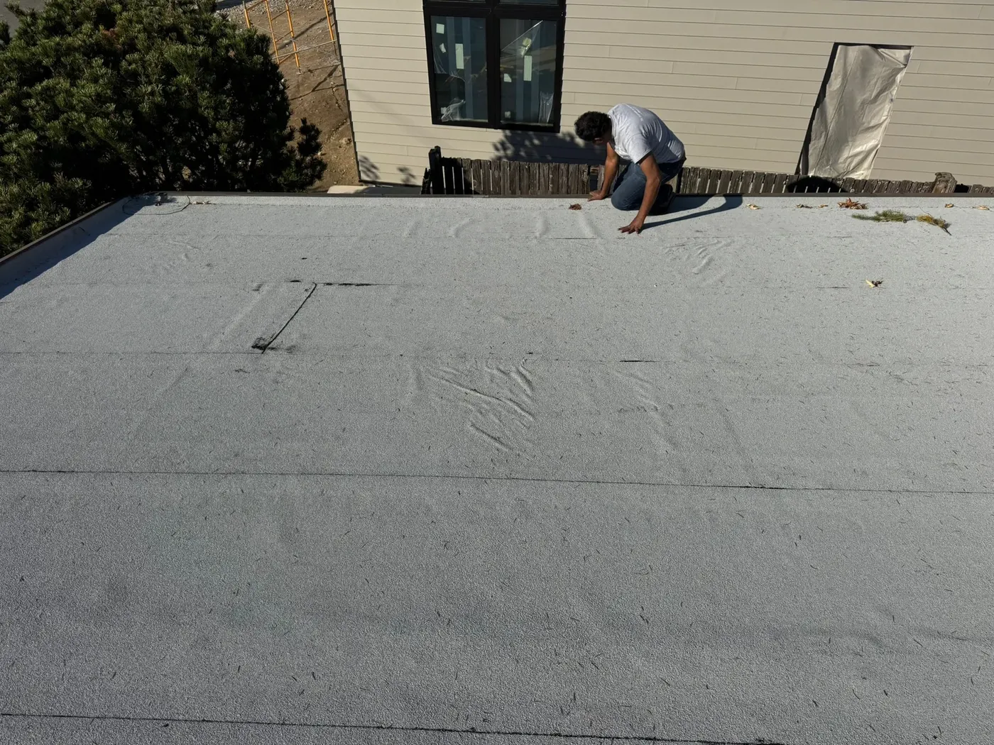 Roofing crew installing new white membrane sheets on a flat residential roof