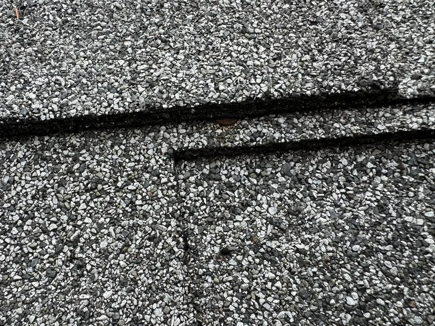 Close-up of a fresh shingle patch repair blended into an existing gray composition roof